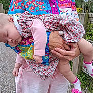 Jacqueline joined the competition — help win amazing prizes! baby, sleeping, child, floral_dress, pink_sleeves, adult_hand, colorful_clothing, outdoor, fence, greenery, grass, pathway, sock, pink_sock, footwear, person, holding, portrait, nature, peaceful