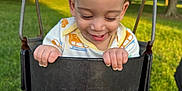 Jayden is registered to the contest to win money with this photo: toddler, child, swing, playground, outdoor, grass, park, smiling, happy, curly_hair, clothing, sunlight, nature, greenery, metal_chains, black_swing, shorts, person, daylight, fun