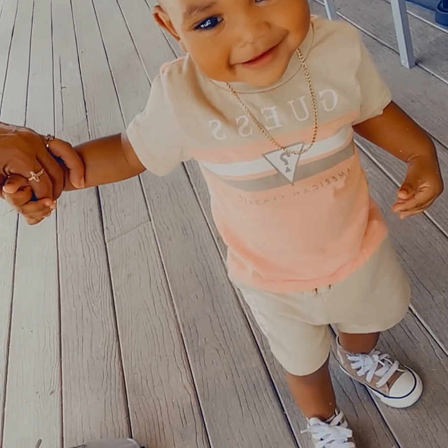 Linzy is registered to the contest to win money with this photo: casual_clothing, chairs, child, cute, daylight, fashion, footwear, happy, holding_hand, necklace, outdoor, person, shorts, smiling, sneakers, toddler, tshirt, walking, wooden_floor, young_child