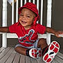 toddler, child, smiling, red_hat, red_shirt, sneakers, white_chair, rocking_chair, gold_chain, casual_clothing, outdoor, happy, cute, portrait, sitting, footwear, person, fashion, accessory, relaxed