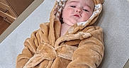 Pj is registered to the contest to win money with this photo: baby, child, robe, hoodie, brown, fluffy, diaper, changing_table, indoor, infant, cute, clothing, person, face, expression, baby_care, soft, toddler, wearing, resting