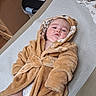 baby, child, robe, hoodie, brown, fluffy, diaper, changing_table, indoor, infant, cute, clothing, person, face, expression, baby_care, soft, toddler, wearing, resting