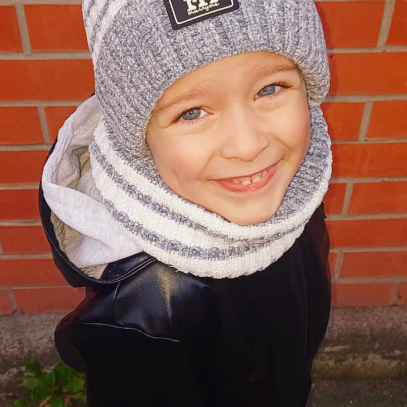 Alenzo a rejoint le concours — aidez-le/la à gagner de superbes lots ! blue_eyes, brick_wall, casual_wear, child, daylight, fashion, happy, hat, jacket, outdoor, person, pom_pom, portrait, scarf, smiling, sneakers, standing, street, warm_clothes, winter_clothing