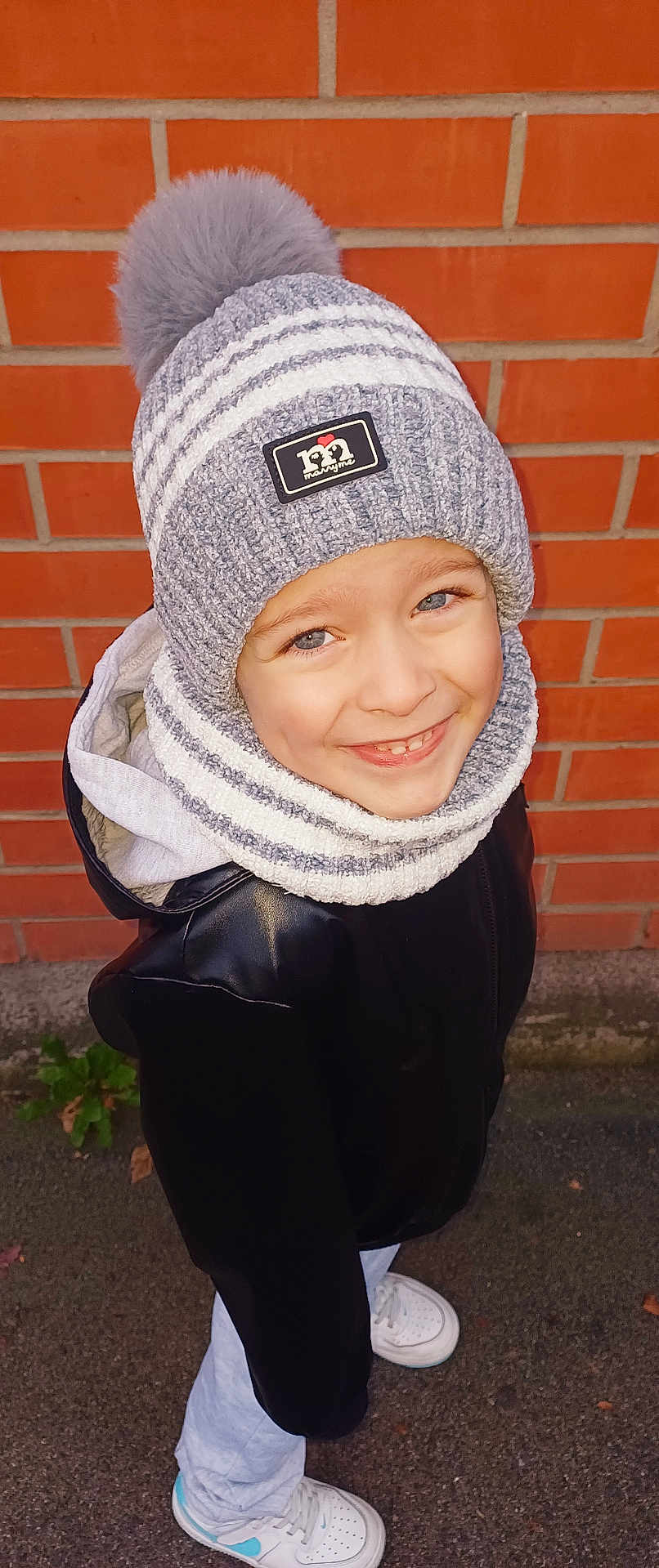 Alenzo a rejoint le concours — aidez-le/la à gagner de superbes lots ! child, smiling, hat, pom_pom, scarf, jacket, sneakers, brick_wall, outdoor, happy, blue_eyes, winter_clothing, street, casual_wear, portrait, person, standing, fashion, warm_clothes, daylight
