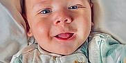 Jaidyn is registered to the contest to win money with this photo: baby, infant, face, blue_eyes, tongue_out, onesie, smiling, lying_down, blanket, cute, child, skin, happy, closeup, young, soft_light, indoors, person, newborn, cozy