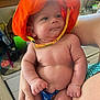 baby, orange_hat, infant, arm, kitchen, person, child, skin, hand, clothing, furniture, indoor, expression, cute, holding, colorful, human, face, portrait, newborn
