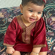 Sultan a rejoint le concours — aidez-le/la à gagner de superbes lots ! baby, child, smiling, traditional_clothing, maroon, hat, bracelet, barefoot, sitting, couch, floral_pattern, indoors, cute, happy, portrait, infant, face, hand, foot, decor