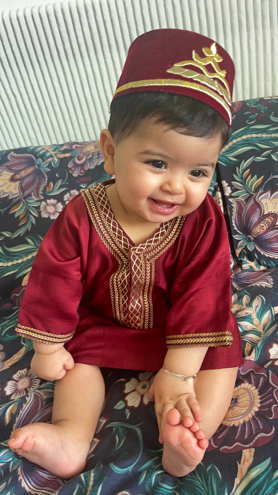 Sultan a rejoint le concours — aidez-le/la à gagner de superbes lots ! baby, child, smiling, traditional_clothing, maroon, hat, bracelet, barefoot, sitting, couch, floral_pattern, indoors, cute, happy, portrait, infant, face, hand, foot, decor