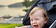 Richard joined the competition — help win amazing prizes! baby, smiling, stroller, child, outdoor, nature, grass, water, lake, trees, happy, pointing, daylight, person, face, blue_eyes, clothing, seatbelt, photography, infant