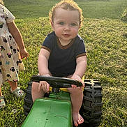 Karter is registered to the contest to win money with this photo: baby, barefoot, blue_eyes, cartoon_print, child, curly_hair, dress, footwear, grass, green, outdoor, person, playtime, steering_wheel, summer, sunlight, toy, tractor, truck, yard