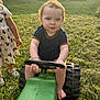 baby, barefoot, blue_eyes, cartoon_print, child, curly_hair, dress, footwear, grass, green, outdoor, person, playtime, steering_wheel, summer, sunlight, toy, tractor, truck, yard