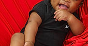 Zaccai is registered to the contest to win money with this photo: baby, infant, child, smiling, black_clothing, sneakers, red_background, happy, cute, portrait, sitting, curly_hair, playful, footwear, one_person, indoors, closeup, baby_shoes, cheerful, toddler