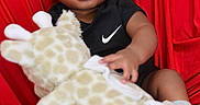 Zaccai is registered to the contest to win money with this photo: baby, black_onesie, child, closeup, curly_hair, cute, giraffe_toy, happy, indoor, infant, nike_logo, playful, plush_toy, portrait, red_background, shoes, sitting, smiling, sock, soft_toy