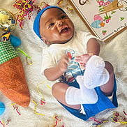 Zaccai is registered to the contest to win money with this photo: baby, blanket, carrot_bag, celebration, child, clothing, confetti, cute, decorations, easter, festive, happy, headband, holiday, infant, laying_down, sign, smiling, sock, toy