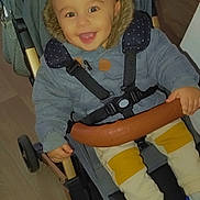 Emilio participe au concours pour gagner de l'argent avec cette photo : baby, baby_carriage, child, clothing, cute, footwear, fur_hood, happy, indoor, jacket, pants, person, seatbelt, smile, sneakers, stroller, toddler, transportation, wooden_floor, young_child