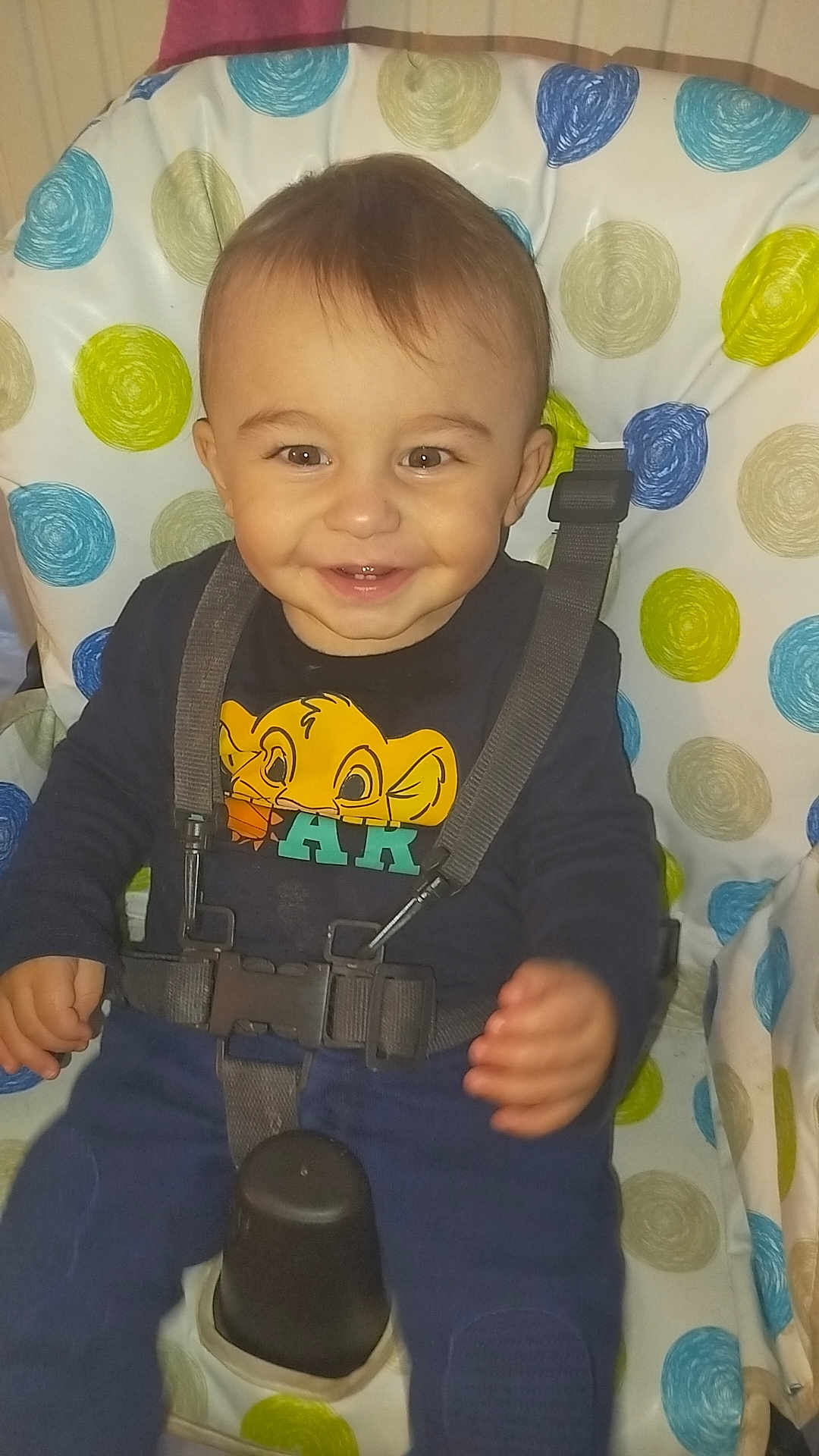 Emilio a rejoint le concours — aidez-le/la à gagner de superbes lots ! baby, child, smiling, high_chair, straps, clothing, face, person, indoor, happy, seat, blue_pants, patterned_cushion, toddler, cute, infant, young_child, expression, sitting, playful