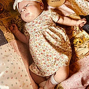 Iris is registered to the contest to win money with this photo: baby, infant, one_month, headband, bow, floral_dress, socks, quilt, patterned_blanket, lying_down, cute, newborn, soft_lighting, indoors, child, portrait, sleepwear, resting, small_hands, peaceful