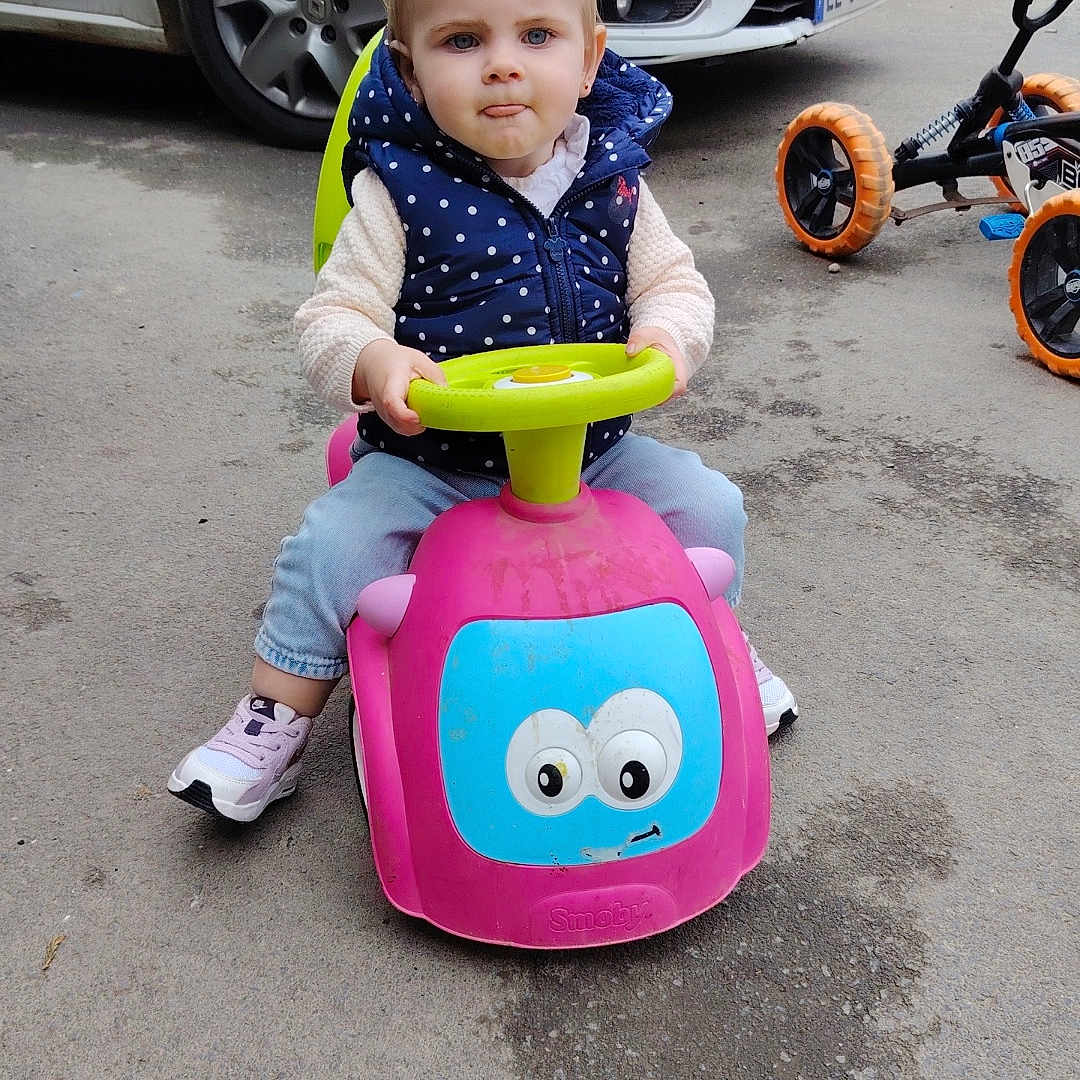 Nélya participe au concours pour gagner de l'argent avec cette photo : blue_eyes, car, child, concentration, cute, jeans, outdoor, parking_lot, pavement, play, polka_dot, ride_on_toy, sneakers, toddler, tongue_out, toy_car, tricycle, vehicle, vest, young_child