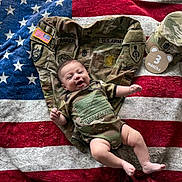 Lucas joined the competition — help win amazing prizes! baby, background, camouflage, clothing, cute, fabric, happy, hat, indoor, infant, jacket, lying_down, military_uniform, patches, person, portrait, smiling, text, three_months, us_flag