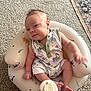baby, infant, onesie, dinosaur_print, pillow, seat, carpet, rug, bottle_top, sitting, chubby_cheeks, happy, face, arm, leg, indoor, newborn, cute, playful, portrait