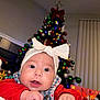 baby, infant, child, headband, bow, christmas_tree, holiday, festive, lights, ornaments, red_sweater, blanket, curious, indoors, decorations, face, hands, cozy, winter, cute