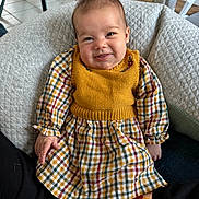 Anna a rejoint le concours — aidez-le/la à gagner de superbes lots ! baby, casual, chair, child, comfortable, cozy, cushion, dress, face, floor, happy, home, indoor, knit_vest, person, plaid, seated, smile, table, wood_floor