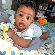 Djelann a rejoint le concours — aidez-le/la à gagner de superbes lots ! baby, blanket, child, christmas_tree, clothing, colorful, curly_hair, cute, decorations, eyes, face, floor, home, indoor, infant, living_room, mouth_open, pillow, television, toy