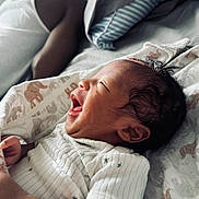 Coa is registered to the contest to win money with this photo: baby, newborn, smiling, blanket, bed, pillow, clothing, infant, face, happy, sleepwear, person, cute, lying_down, indoors, soft_light, closeup, skin, head, young_child