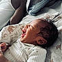 baby, newborn, smiling, blanket, bed, pillow, clothing, infant, face, happy, sleepwear, person, cute, lying_down, indoors, soft_light, closeup, skin, head, young_child