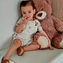 Anes participe au concours pour gagner de l'argent avec cette photo : toddler, child, plush_toy, teddy_bear, white_overalls, brown_sandals, finger_in_mouth, curious_expression, indoor, changing_table, minimalist_room, wood_panel, white_wall, sitting, cute, soft_lighting, comfortable, young_child, person, portrait