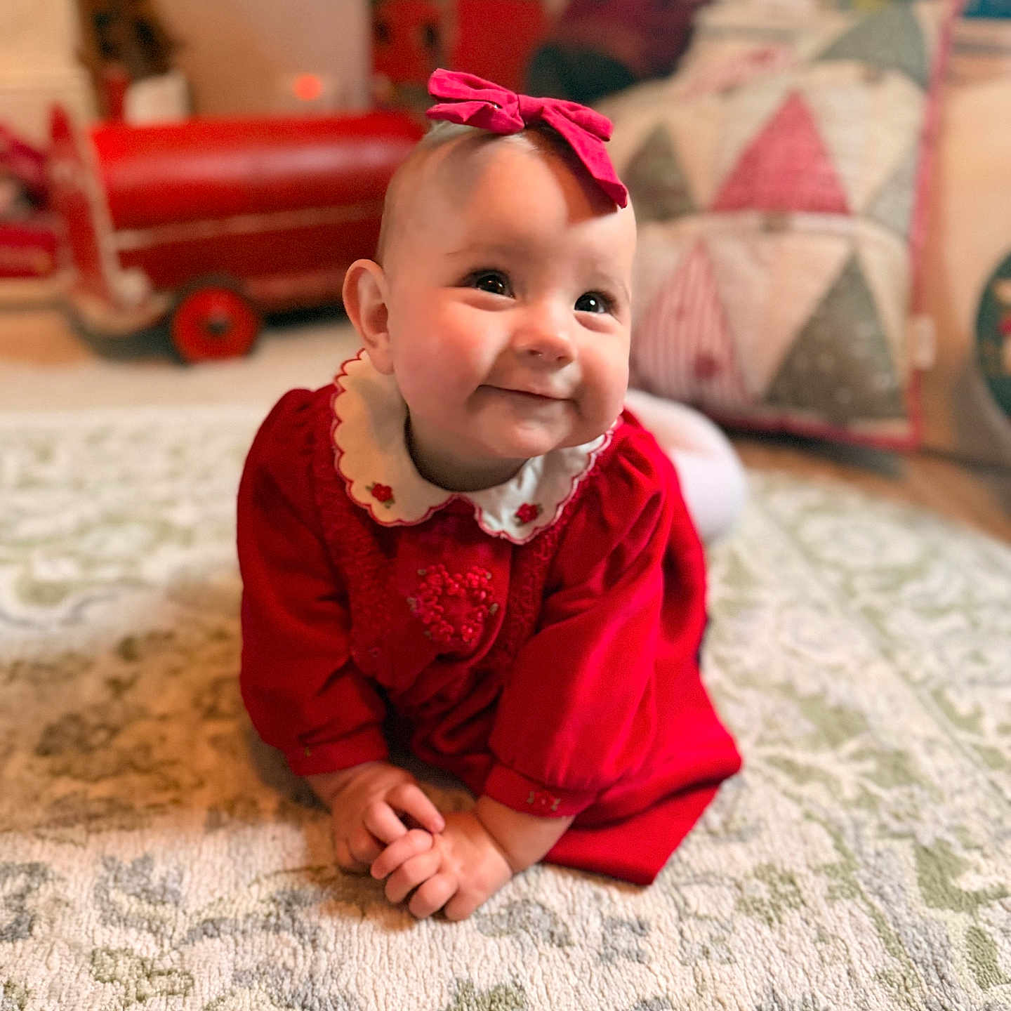 Hattie-Bloom joined the competition — help win amazing prizes! baby, bow, carpet, child, cozy, crawling, cute, decor, happy, home, indoors, infant, patterned_rug, person, pillow, portrait, red_dress, smiling, toy_car, warm_lighting