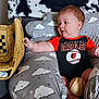 baby, child, baseball, baseball_glove, onesie, cushion, cloud_pattern, infant, indoor, curious, sports, soft_furniture, sitting, cute, red_hair, hand, toy, comfort, playful, person
