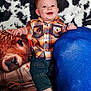 baby, barefoot, blue_cushion, child, colorful, cow_print, cozy, cushion, cute, denim_pants, fabric, happy, indoor, infant, person, plaid_shirt, plush, portrait, seated, smiling