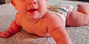 William is registered to the contest to win money with this photo: baby, infant, diaper, bed, blanket, skin, arm, face, eyes, mouth, cheeks, person, lying_down, curious, reaching, indoors, soft_light, texture, stacked_blankets, closeup