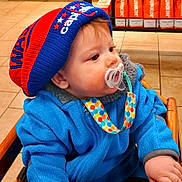 William is registered to the contest to win money with this photo: baby, blue_hat, blue_jacket, child, closeup, coffee_bags, colorful, cute, dunkin, floor_tiles, high_chair, indoor, infant, knit_hat, pacifier, polka_dot, portrait, red_hat, seated, warm_clothing