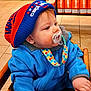 baby, blue_hat, blue_jacket, child, closeup, coffee_bags, colorful, cute, dunkin, floor_tiles, high_chair, indoor, infant, knit_hat, pacifier, polka_dot, portrait, red_hat, seated, warm_clothing