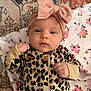 baby, infant, headband, leopard_print, onesie, pink_bow, blanket, floral_pattern, rug, fist, face, lying_down, indoor, child, cute, expression, clothing, portrait, young, person