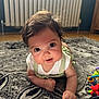 baby, infant, child, cute, face, eyes, hair, rug, floor, toy, home, indoor, crawling, clothing, white_shirt, green_overalls, curious, smiling, closeup, portrait