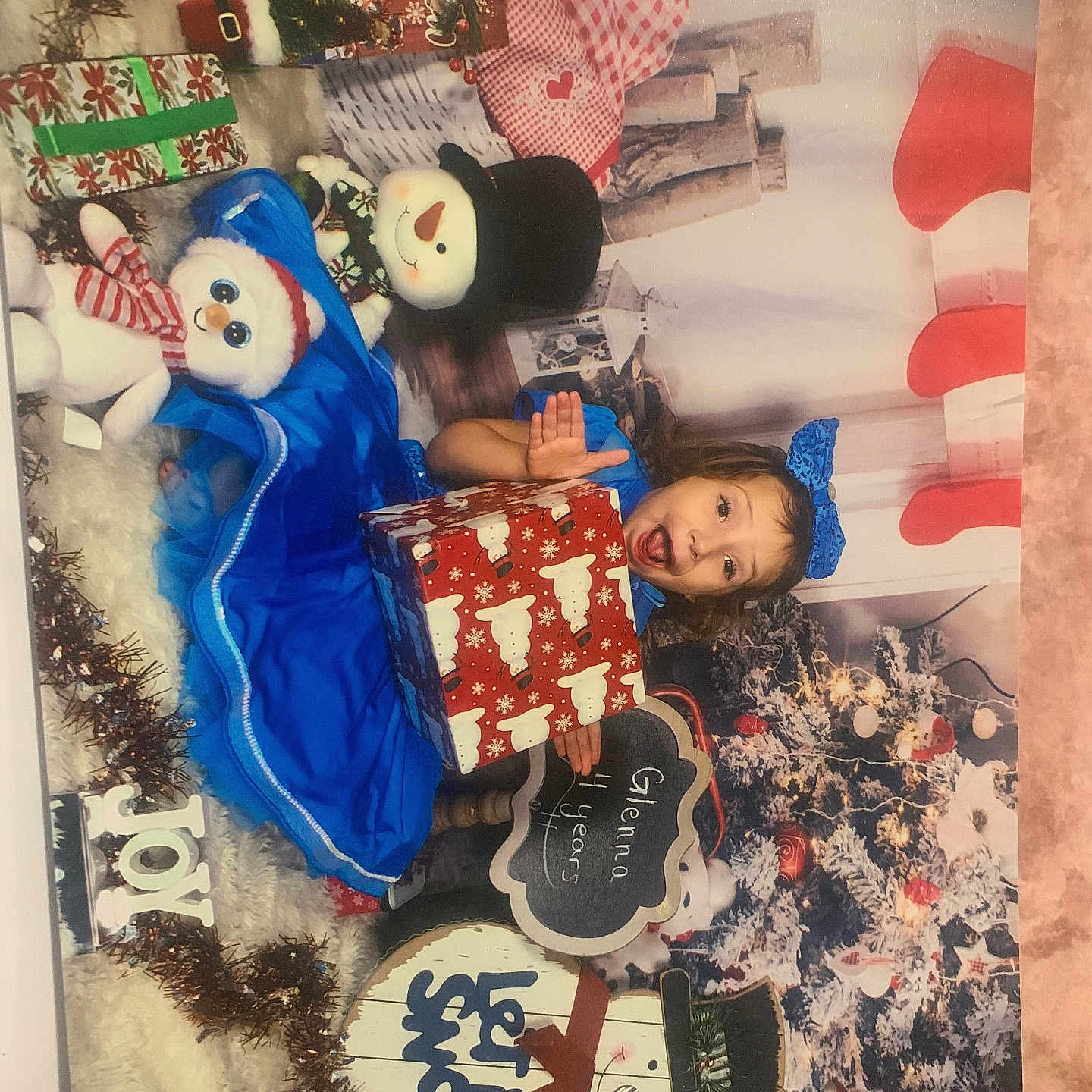 Glenna is registered to the contest to win money with this photo: blue_dress, bow, celebration, chalkboard_sign, child, christmas_tree, decorations, festive, gift_box, girl, holiday, holiday_photo, holiday_season, holiday_sign, indoors, joy, let_it_snow, plush_toy, smiling, snowman