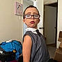 child, glasses, makeup, lipstick, eyebrows, sweater_vest, tie, indoor, room, laundry_basket, clothes, door, cardboard_boxes, carpet, wall_art, person, portrait, fashion, expression, posing