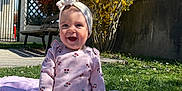 Amelia a rejoint le concours — aidez-le/la à gagner de superbes lots ! baby, bench, blanket, blue_sky, child, concrete, fence, flowering_bush, garden, grass, happy, headband, outdoor, pink_clothing, rattle, smile, sock, sunlight, toy, yellow_flowers