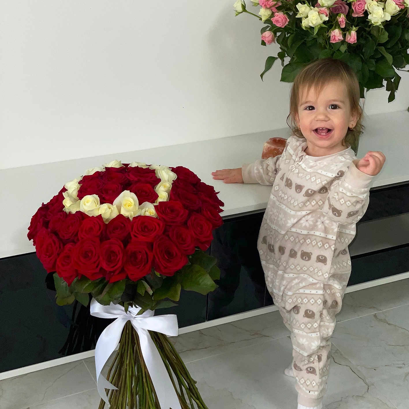 Amelia a rejoint le concours — aidez-le/la à gagner de superbes lots ! bouquet, cabinet, child, cute, decor, floor, flowers, green_leaves, happy, heart_shape, indoor, marble_floor, pajamas, person, plant, roses, smiling, standing, toddler, white_ribbon