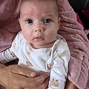 Mila joined the competition — help win amazing prizes! baby, infant, onesie, sheep_pattern, blanket, pink, hands, adult, holding, skin, face, eyes, expression, indoor, clothing, person, couch, comfort, portrait, cute