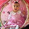 adorable, baby, bird, bow, canopy, child, colorful, curious, cute, decor, face, flower, grass, headband, indoor, pink_dress, playful, portrait, seated, young_child