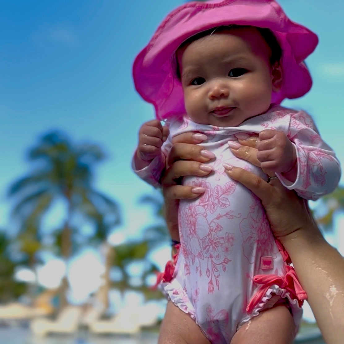 Liviana is registered to the contest to win money with this photo: baby, child, cute, hands, holiday, infant, legs, outdoor, palm_trees, person, pink_hat, pool, portrait, skin, smiling, summer, sunlight, swimsuit, vacation, water