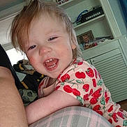 Chloe is registered to the contest to win money with this photo: toddler, child, smiling, happy, indoor, plaid, cushion, furniture, cabinet, hair, face, person, clothing, pattern, red, pink, home, living_room, laughing, cute