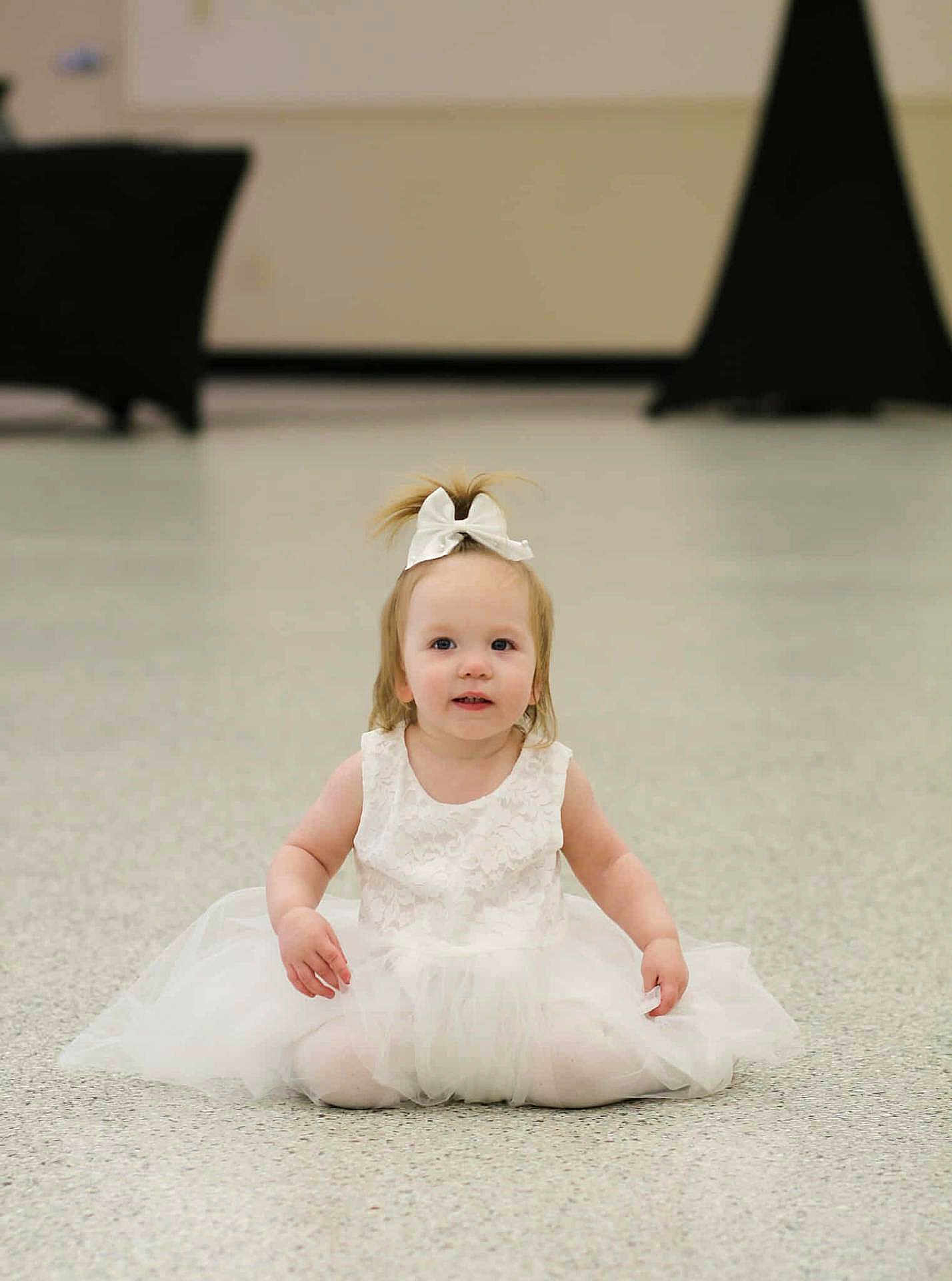 Chloe is registered to the contest to win money with this photo: toddler, child, white_dress, bow, sitting, floor, indoor, curious, smile, blonde_hair, young_child, portrait, cute, fashion, girl, innocence, soft_lighting, background_blur, person, baby
