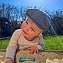 child, toddler, sandbox, sand, hat, cap, sunlight, outdoor, grass, smile, happy, face, hand, toy, play, backyard, sunflare, blue_sky, cloud, cheek