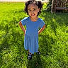 child, girl, smiling, portrait, outdoors, garden, grass, blue_dress, curly_hair, sunlight, standing, hands_on_hips, playful, happy, bench, trees, lawn, road, shoes, nature