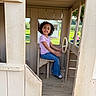 Serenity is registered to the contest to win money with this photo: child, smiling, playhouse, toy_vehicle, steering_wheel, sitting, outdoors, playground, wooden_structure, portrait, curly_hair, striped_shirt, jeans, shoes, green_grass, rural, daylight, window, family_activity, happy